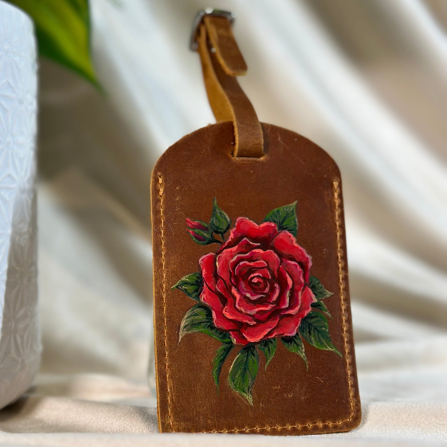 Brown leather luggage tag with a red rose design on a light background