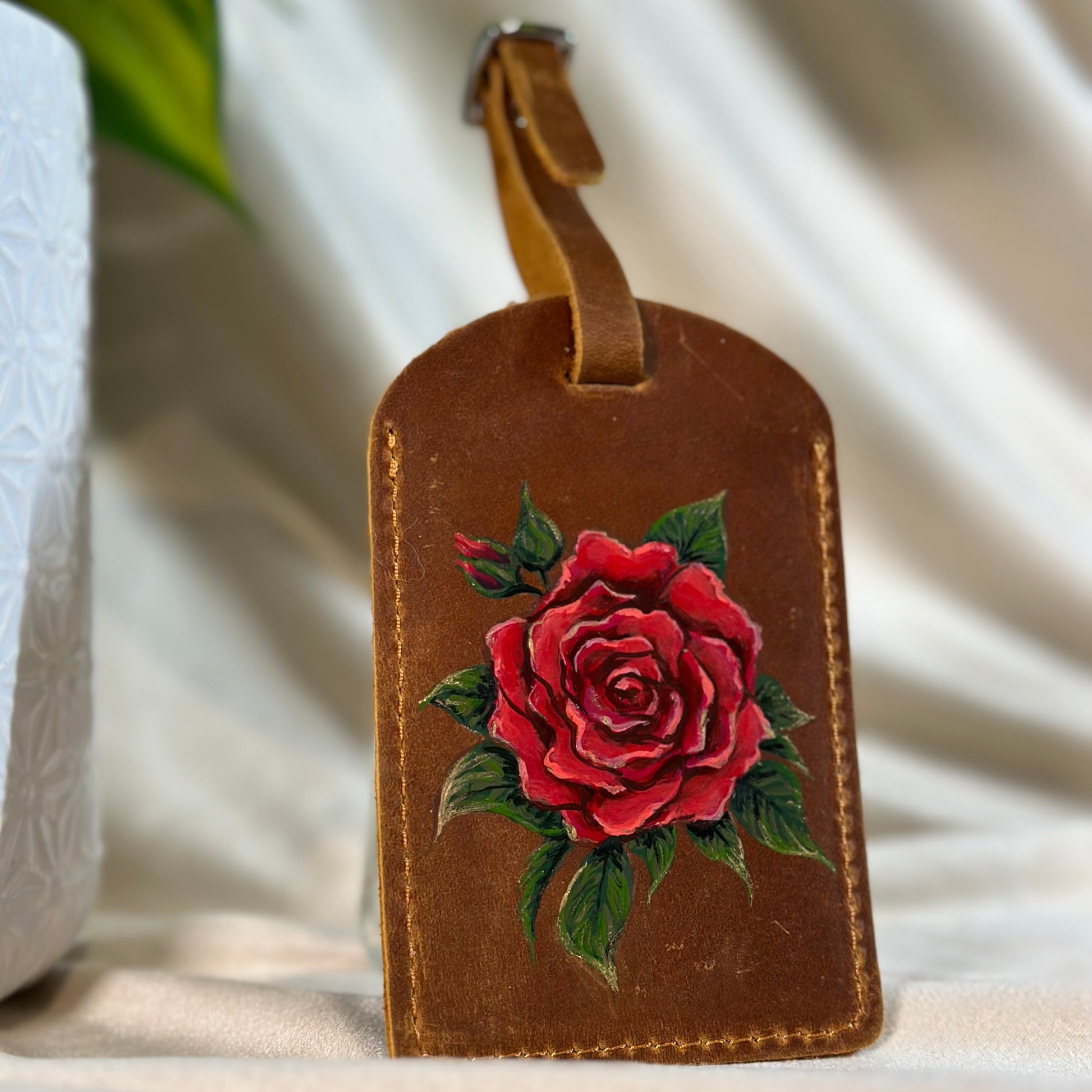 Brown leather luggage tag with a red rose design on a light background